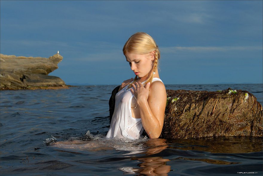 Светловолосая девушка в сырой майке купается в воде