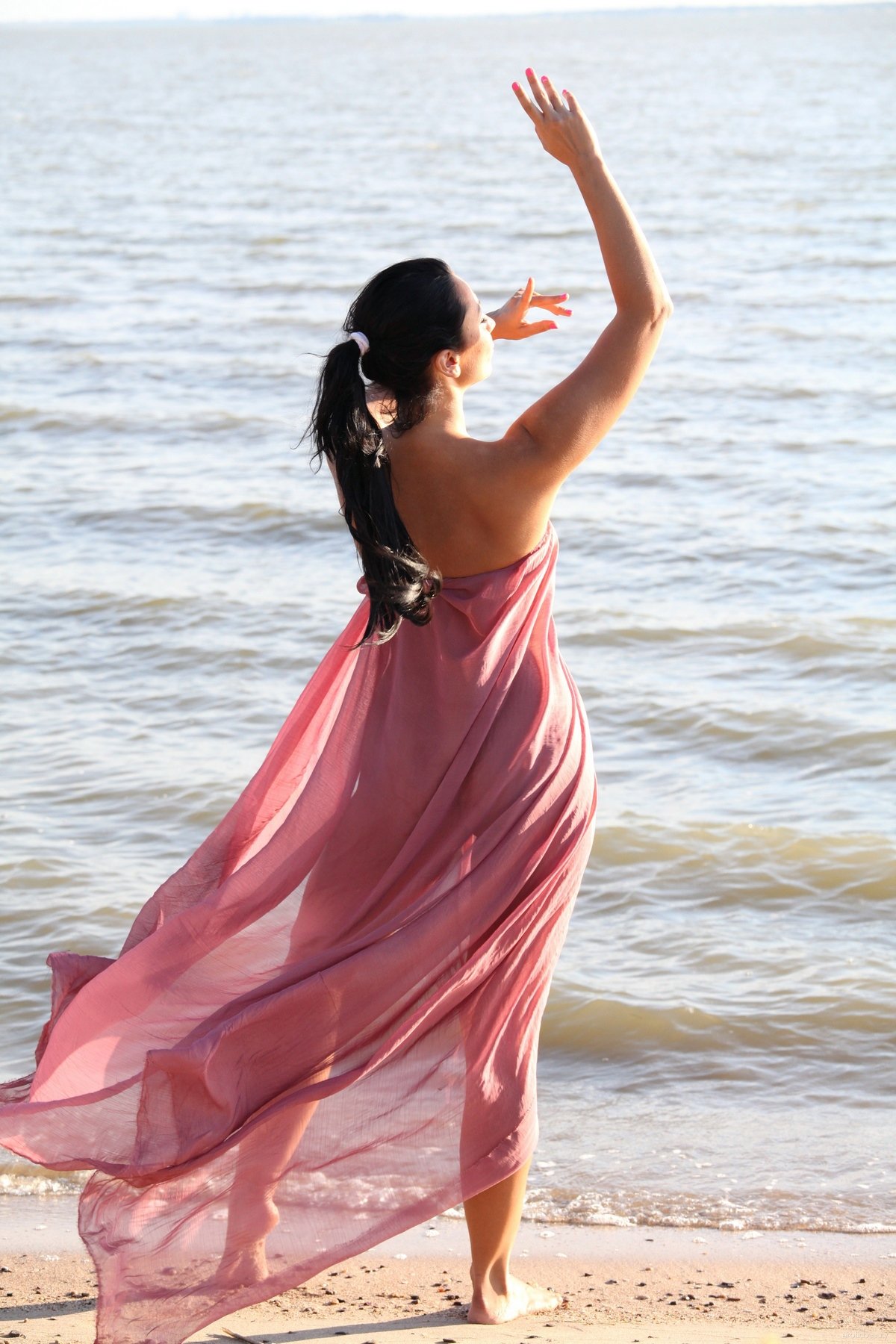 Брюнетка с женственной фигурой играет с парео на берегу реки